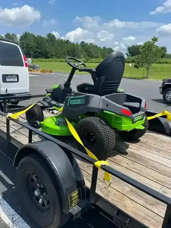 A Greenworks Pro riding mower strapped to the Rich Sity Hauling trailer under a clear sky