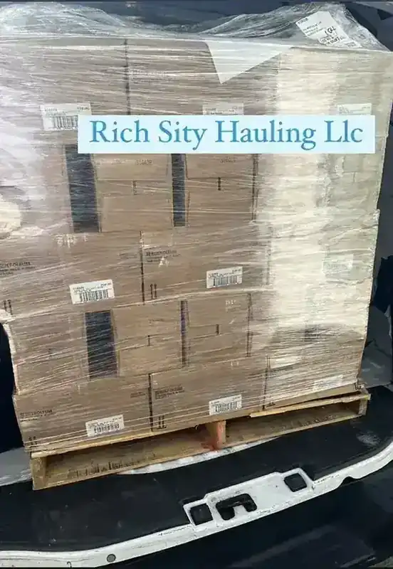 A shrink-wrapped pallet of stock loaded in a Rich Sity Hauling truck bed for delivery