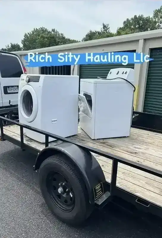 A washer and dryer strapped to the Rich Sity Hauling trailer outside a row of storage units